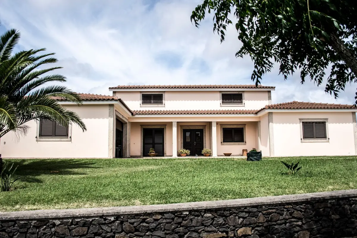 A cream stucco house with a tile roof, a green lawn and a palm tree